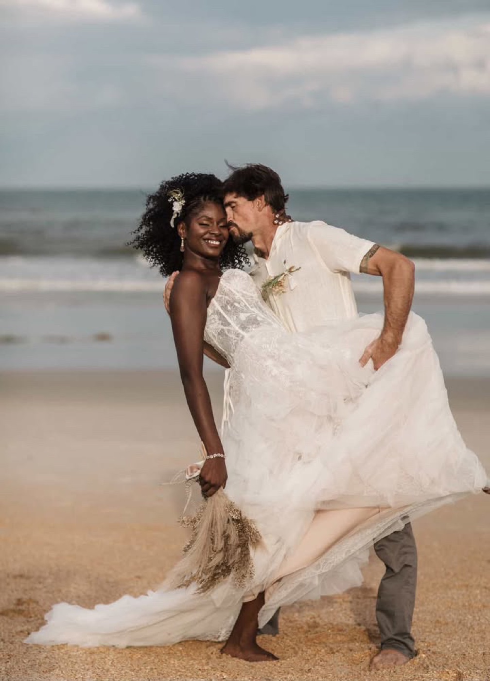 Couple barefoot on the beach in wedding attire, windswept curls